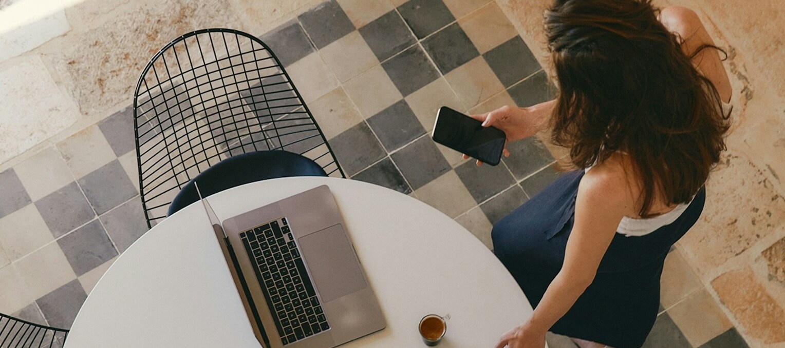 Persona cerca de una mesa con un ordenador y mirando un movil